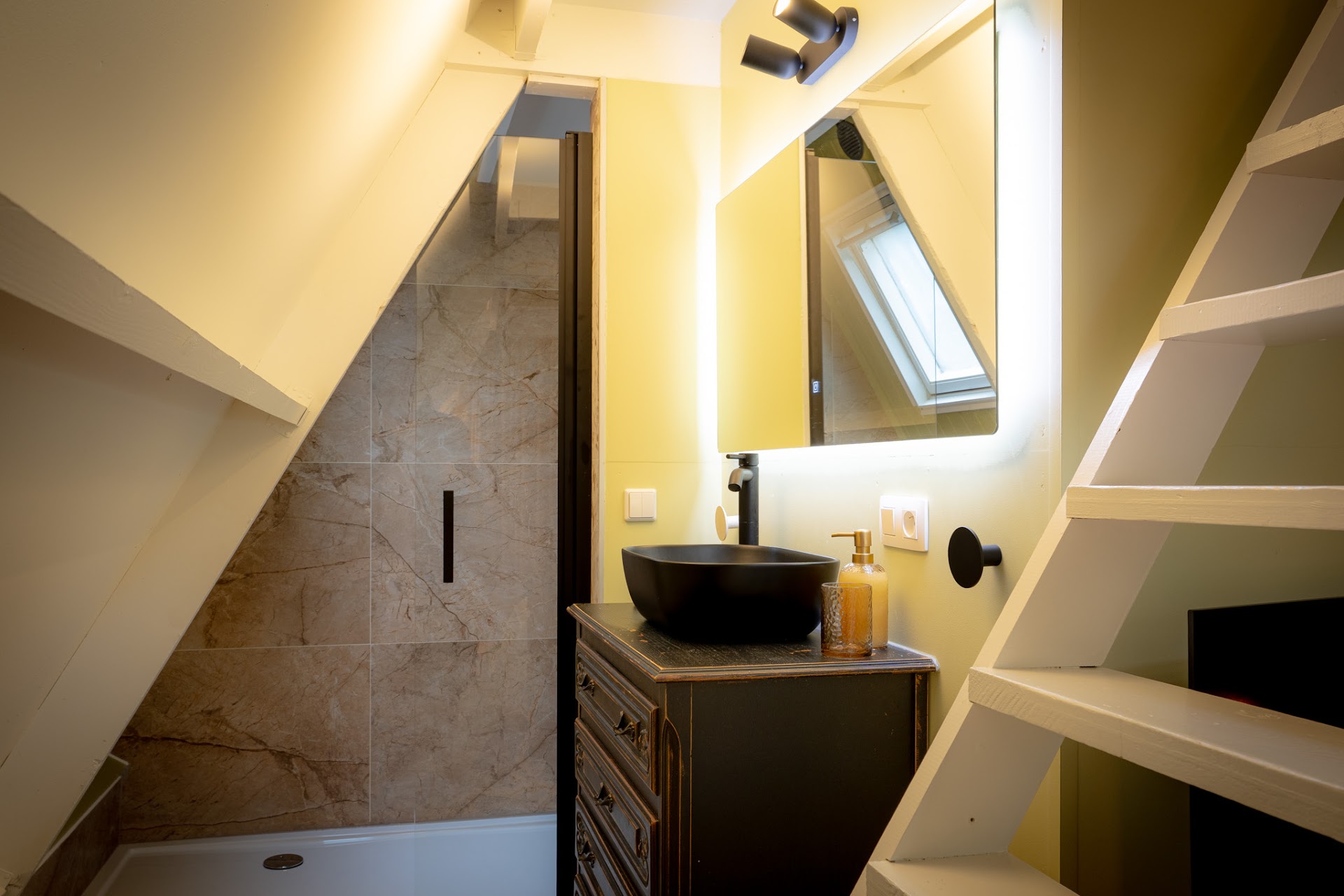 Badkamer met wastafel, spiegel en douche onder een schuin dak
